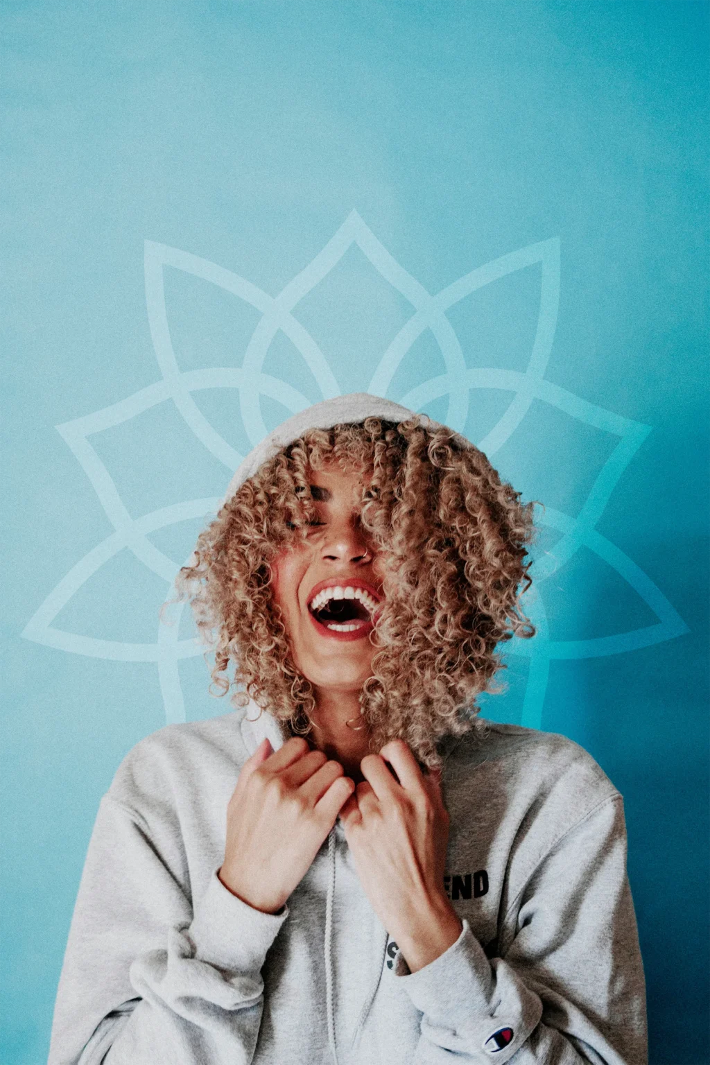 Happy young woman laughing wearing a sweatshirt, in front of a blue wall with a Pure Vitality logo imprinted behind her head