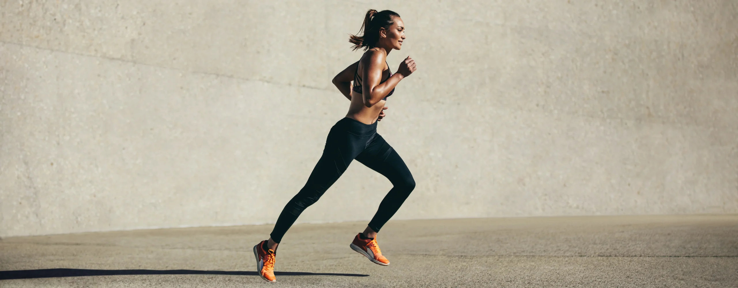 Healthy woman running in black workout outfit with orange shoes